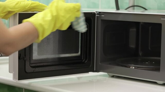 A woman's hand washes a white microwave oven in the kitchen