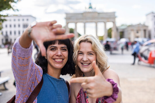Happy female friends make a frame gesture at Brandenburg Gate