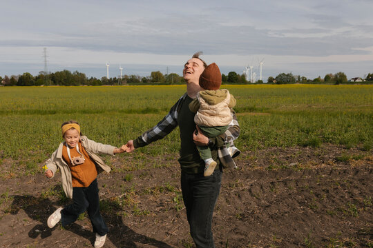Father walks with his children in a field near a wind turbine