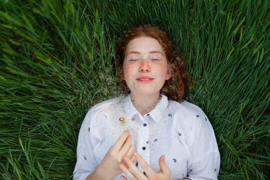 Woman with red hair relaxes in the grass with a dandelion