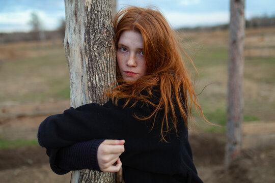 Portrait of teenage girl with red hair and freckles hugging a tree outdoors