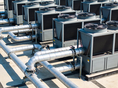Industrial HVAC units with large metal pipes on a rooftop under bright sunlight