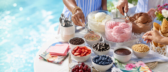 Summer pool party ice cream buffet with various toppings beside a pool background © dvoevnore
