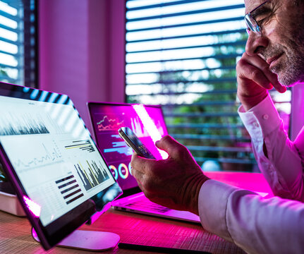 Businessman checks financial data on smartphone in neon lit office