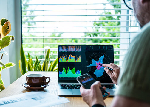 A man analyzes business data on a laptop and smartphone in an office