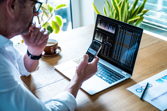 Man analyzing financial data on notebook and smartphone indoors