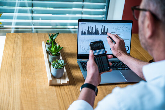 A broker analyzes financial data on a notebook and smartphone screen