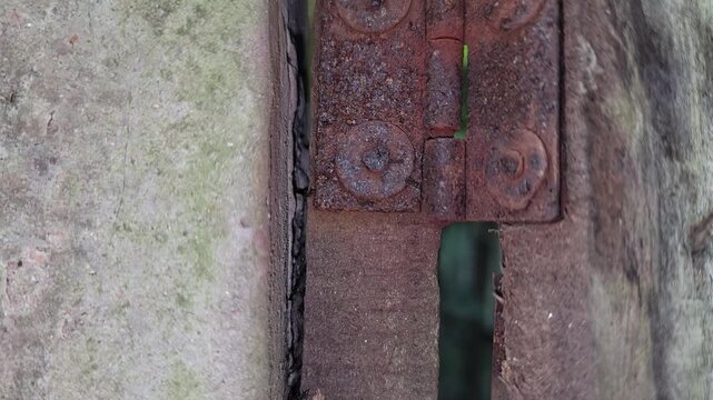 A close up of a heavily rusted metal hinge attached to an old wooden frame