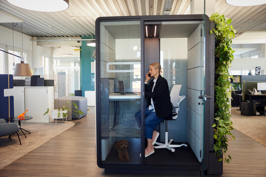 Woman talks on smartphone inside modern office telephone booth