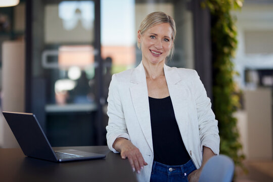 Confident business woman smiles near a laptop in a modern office