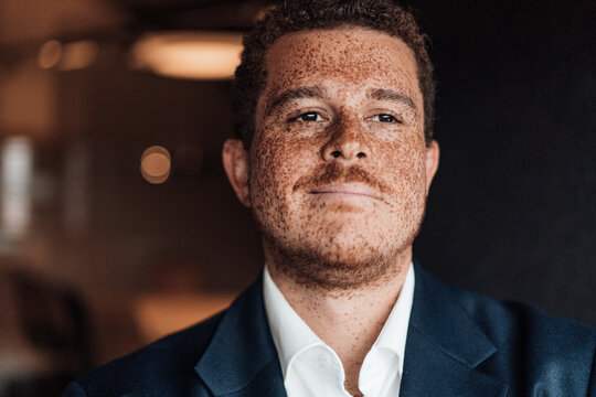 A confident businessman with freckles smiles in the dark office