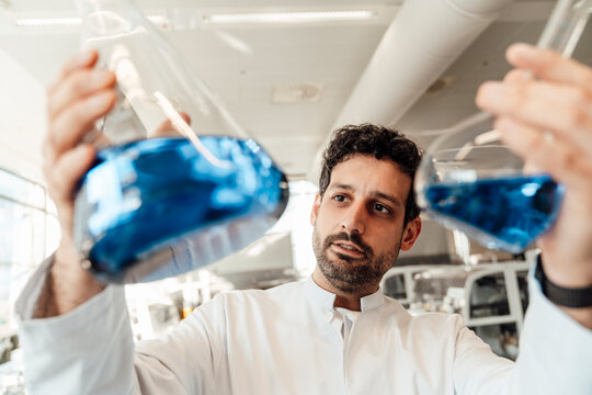 Scientist examining blue liquid in glass flask in laboratory