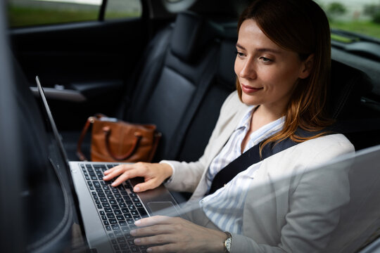 Businesswoman works on laptop in car during travel