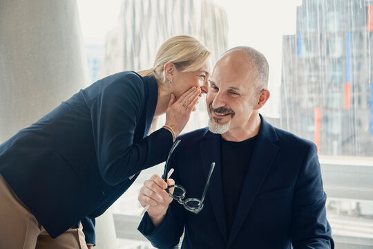 A businesswoman whispers a joke to her male colleague at the office