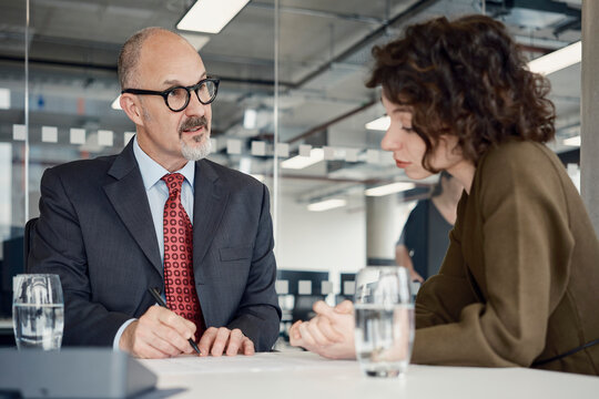 A businessman and a businesswoman discuss work at an office desk