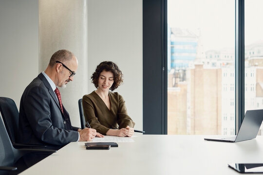 Businessman and businesswoman sign contract at London office desk