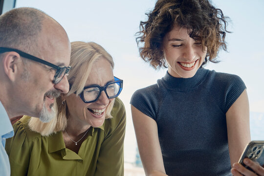 Happy colleagues looking at a smartphone during an office meeting