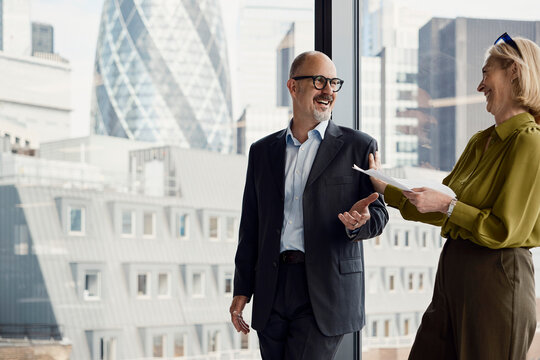 Businessman and businesswoman discuss work by a London office window