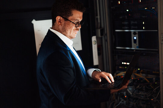A male technician types on a laptop near a network cabinet