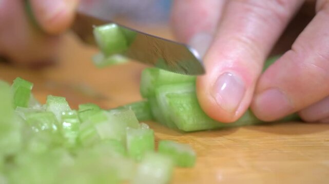 Fresh celery stalks are sliced to reveal their crisp and fibrous texture on the cutting board, the vibrant green color and freshness adding life to this essential soffritto ingredient.