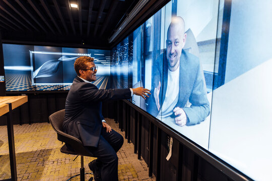 Smiling businessman reaches for virtual handshake on huge screen
