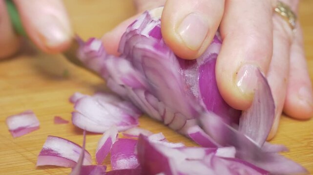 A knife slices cleanly through a fresh onion on a wooden cutting board, preparing the pungent and essential element of the classic Italian soffritto base for a rich homemade sauce.