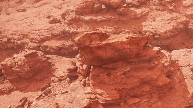 The scene shows a rocky area on Mars with various stones and dusty ground. The landscape appears dry and uneven. Sunlight casts shadows on the rough textures of the surface.