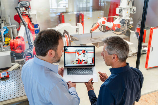 Colleagues discuss an industrial robot on a laptop in a factory