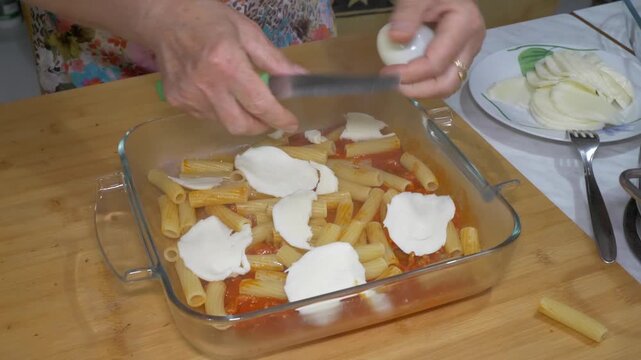 Careful hands place scamorza slices one by one over a tray of pasta, a loving and methodical gesture that reflects the deep pride and tradition behind southern Italian baked pasta.