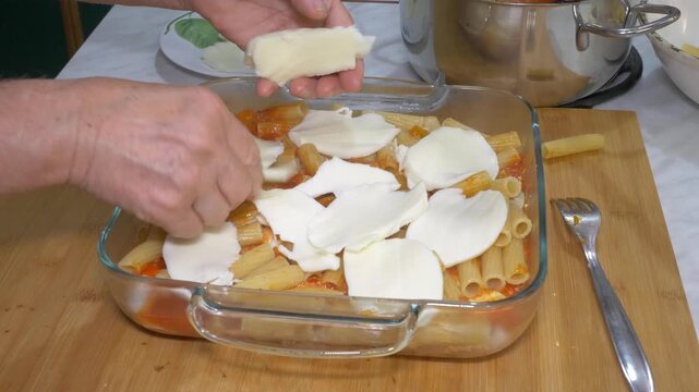Slices of fresh scamorza cheese are carefully laid over pasta in a baking tray, building the classic layers of a beloved southern Italian baked pasta dish ready for the oven.