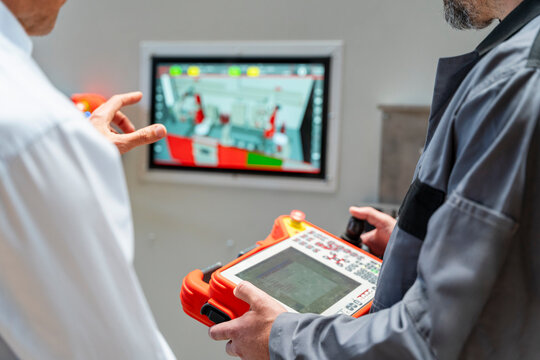 Male engineers inspect industrial robots on a control screen