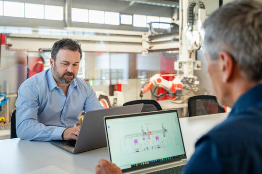 Mature engineer and manager planning production on laptop in factory