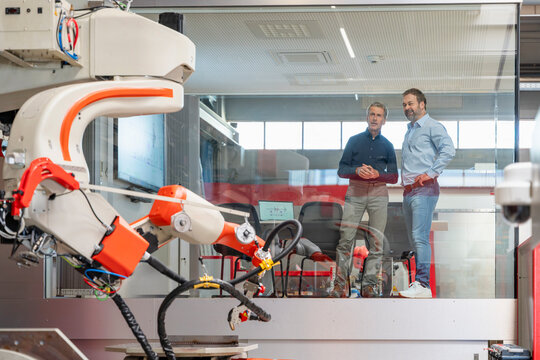 Male colleagues observe an industrial robot in a factory office