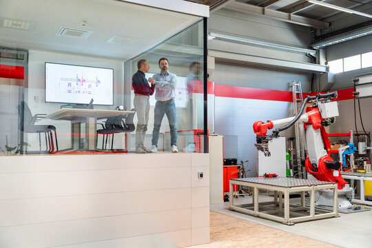 Male engineers discuss automation inside a glass factory office