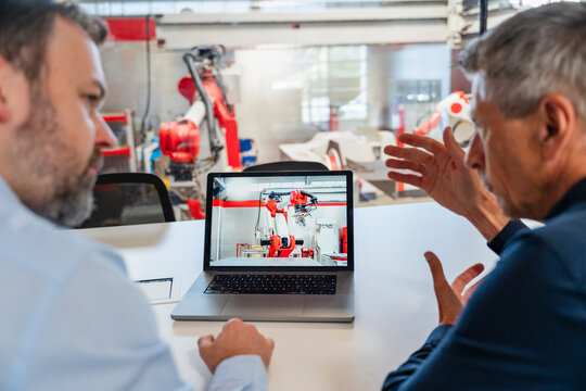 Male engineer discusses industrial robot on laptop with colleague