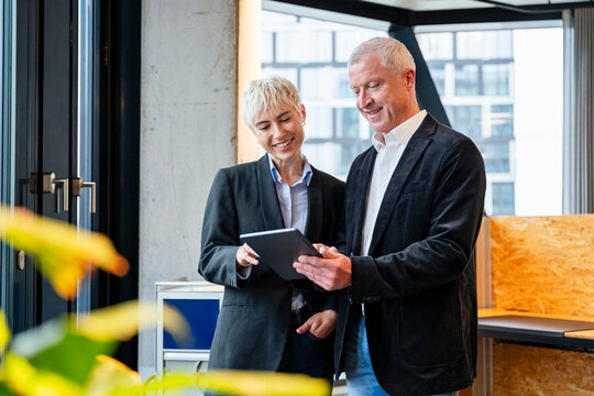 Smiling colleagues planning with tablet in modern office