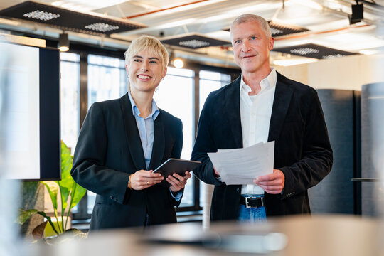 Businessman and businesswoman holding tablet and document in office