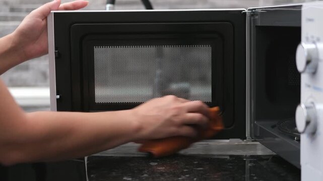 A woman's hand washes a white microwave oven in the kitchen