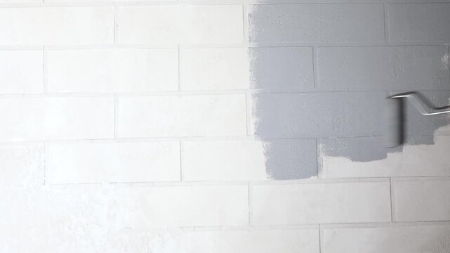 Close-up of a hand painting a white brick wall grey with a paint roller