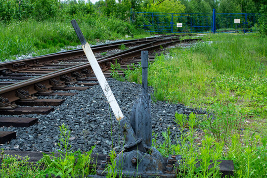 Manual railway switch handle next to train tracks. Metal infrastructure device for controlling rail direction. Transportation equipment for changing route. Industrial train track segment.