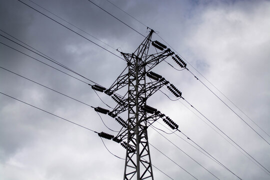 Electricity pylon against a cloudy grey sky. High voltage transmission tower with power lines. Grid infrastructure for energy distribution and industrial power supply sustainability.
