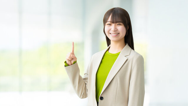 人差し指を立てて案内する若い女性・ビジネスウーマン