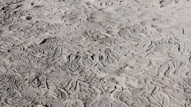 A high-angle, close-up shot of multiple overlapping shoe print impressions in dry, textured sand, illustrating a busy path or high-traffic area.