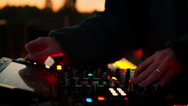 dj mixing music on plastic turntables at sunset over-the-shoulder shot with red and yellow headphones and electronic equipment in a vibrant outdoor event setting.