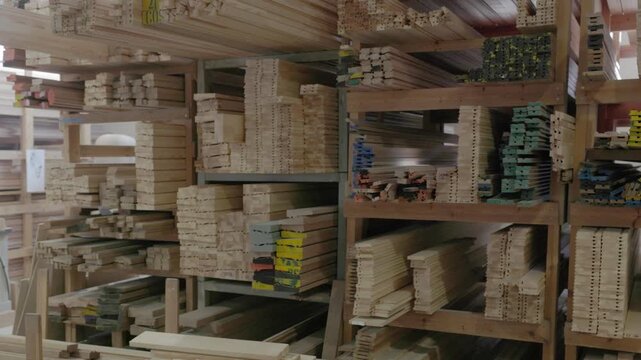 Stacked wooden profiles with marked measurements stored on factory shelving for window frame production