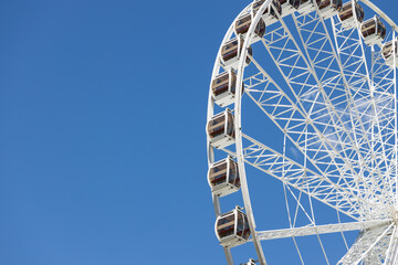 Giant Ferris wheel with cabins against a clear blue sky on a sunny day © Artem Kniaz