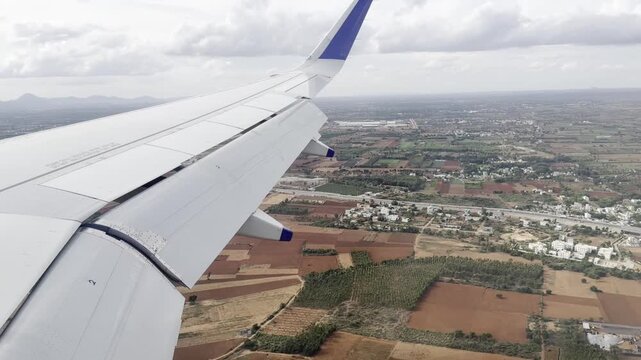 Full HD aerial footage from an airplane window showing the aircraft wing above patchwork farmland, rural roads and village buildings, capturing scenic flight travel and countryside landscape below.