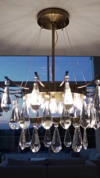 Vertical video: Tilting camera revealing chandelier above living area at dusk, showing crystals