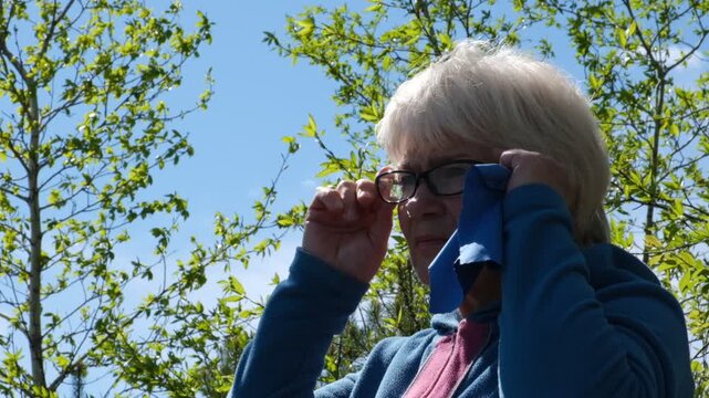 Senior woman is carefully wiping her eyeglasses with a soft microfiber cloth. themes of daily routine, care for personal items, and the quiet dignity of mature age. 