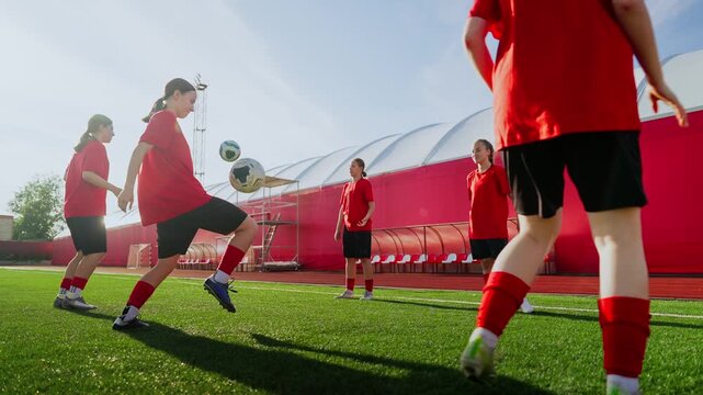 Women's soccer training session with players in red jerseys practicing ball control, passing drills, and teamwork on a sunny outdoor field with artificial turf